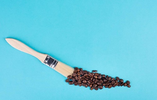 Painting with a brush a line with roasted coffee beans, blue background with copy space, having a