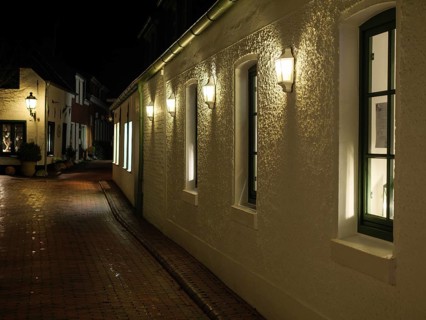 A dark street at night with white, illuminated buildings and cobblestones under streetlights,