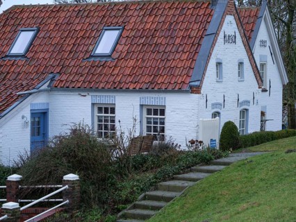 A white farmhouse with a red tiled roof and a staircase surrounded by grass and shrubs in a rural