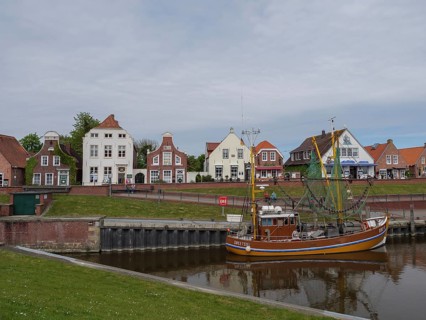 Houses line the harbour where a fishing boat is anchored in the calm water, Greetsiel, East Frisia,