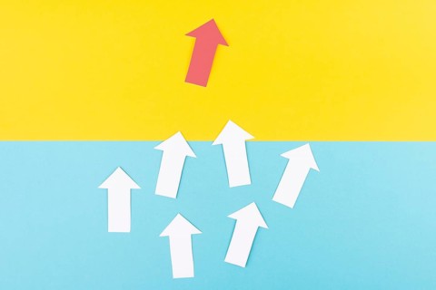 White arrows on a green background, one red is standing out, do different, be a winner,
