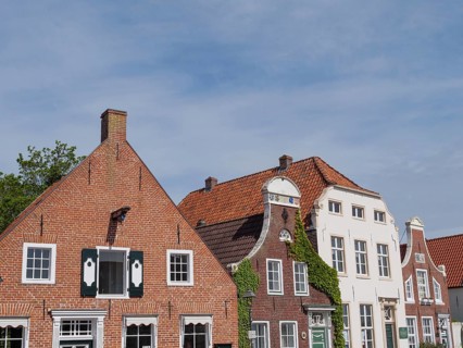 Historic brick houses with gabled roofs and plastered facades under a clear sky, greetsiel, east