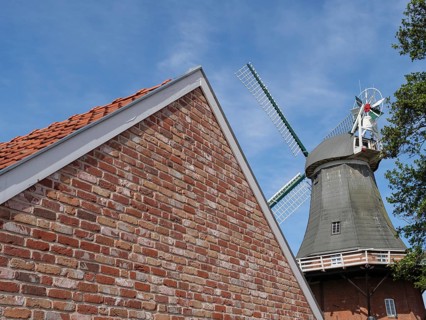 Brick building with the top of a windmill in the background under a blue sky, Greetsiel, East
