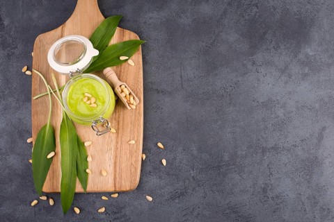 Pesto made from wild garlic, pine nuts and feta cheese in a glass, with fresh leaves on a dark