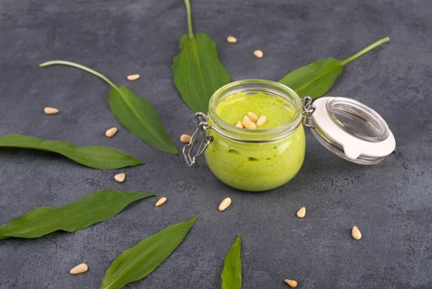 Pesto made from wild garlic, pine nuts and feta cheese in a glass, with fresh leaves on a dark