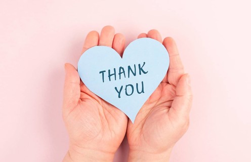 Holding a heart with the words thank you in the hands, pink colored background, greeting card,