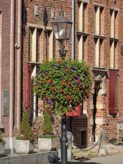 A colourful display of flowers hanging from a lamppost in front of a historic brick building with