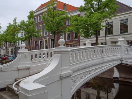 White decorative bridge over a canal, surrounded by houses and green trees, Delft, Holland,