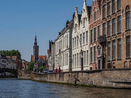 Historic buildings and a church tower along a canal with detailed architecture and blue sky,