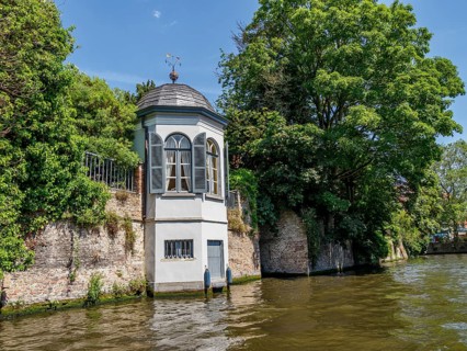 Small riverside pavilion surrounded by lush vegetation and calm water, Bruges, Flanders, Belgium,
