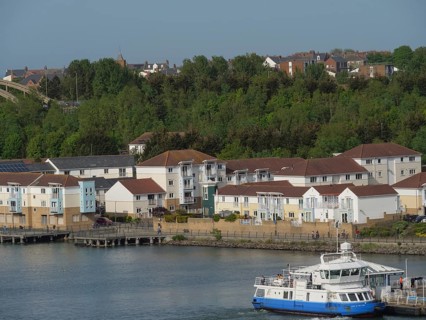 Residential area with a ferry in the foreground, surrounded by green spaces and the harbour,