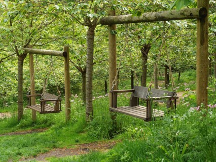 Two wooden garden swings hanging from a frame in the forest under green trees, Thynemouth, England,