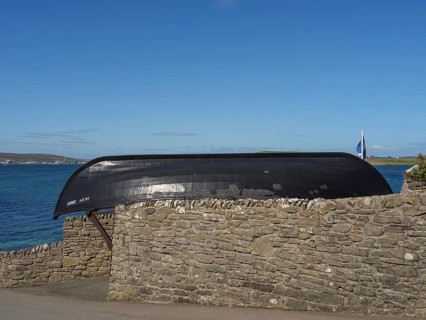 An old black boat rests on a stone wall with sea views and clear skies, lerwick, shetlands,