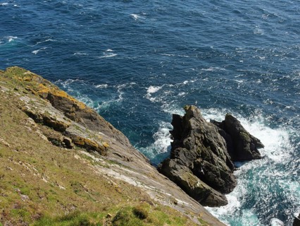 Steep cliffs meet turbulent blue seawater with white spray waves, lerwick, shetlands, scotland,