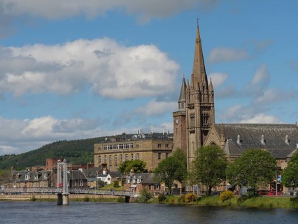 Large church tower and municipal buildings next to a bridge over a river with blue sky and clouds,