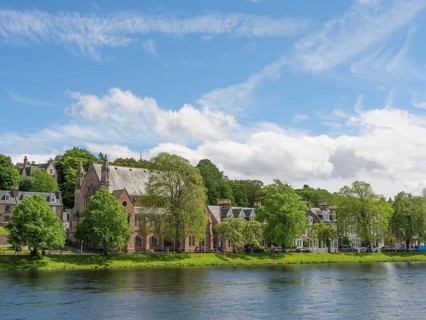 View of a picturesque row of houses and a church along a river with blue sky and white clouds,