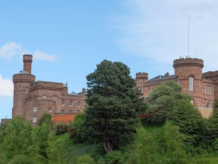 A large castle on a green hill, surrounded by trees and under a blue sky, inverness, scotland,