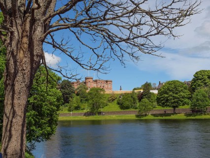 A castle on a hill on the banks of a river, surrounded by trees and under a blue sky, inverness,