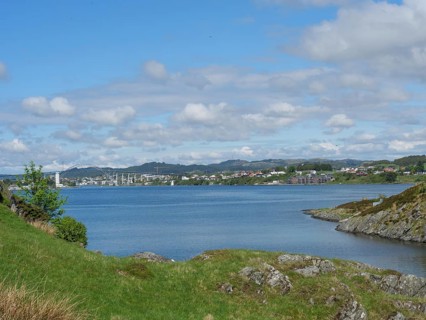 A calm lake surrounded by green hills and houses under a partly cloudy sky, haugesund, norway,