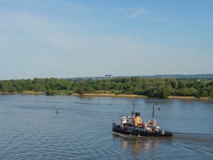 A steamboat sails on a calm river under a clear sky with green banks, Elbe, Hamburg, Northern