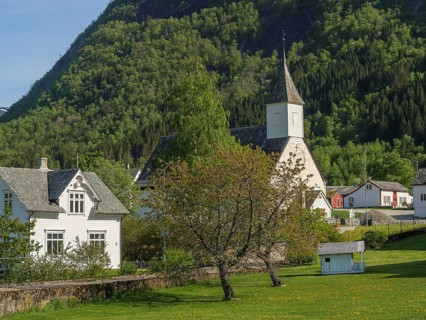 White church building in a green village, surrounded by trees and mountains, on a sunny spring day,