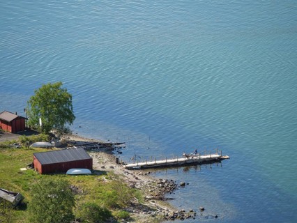 Calm lake scene with jetty and small red huts on the shore, clearly depicted water and nature,