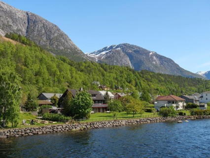 A small village with houses along a river against the backdrop of high mountains and a clear sky,
