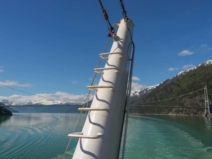 View from the deck of a ship with a view of mountains and a bridge over the water under a clear