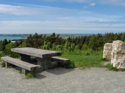 Wooden table and bench on a gravel path with a view of the forest and sea under a slightly cloudy