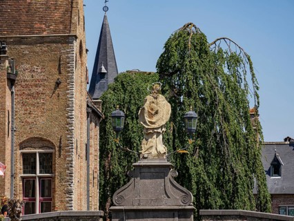 Statue in the foreground in front of historic brick buildings, a church with spire and gardens,