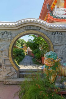 A decorative stone arch with a sculpture of a lion in a traditional temple garden with surrounding