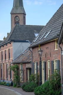 A peaceful village street with a view of the church tower, surrounded by old brick houses, planted