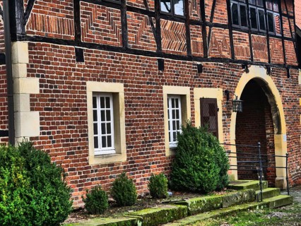 The entrance of a half-timbered house with brick walls, white windows and green bushes, asbeck,