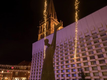 Statue in front of an illuminated church at night with fairy lights creating a festive atmosphere,