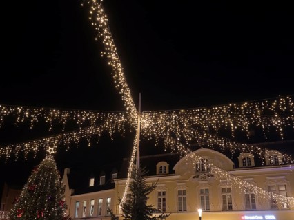 Festively illuminated scenes at night with fairy lights above a building and Christmas decorations,
