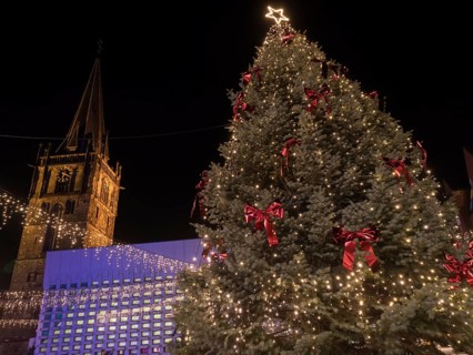 In the centre a large, festively decorated Christmas tree with lights, red bows and a star at the