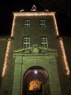 Brick entrance area of a district court with illuminated arch and fairy lights at night, Ahaus,