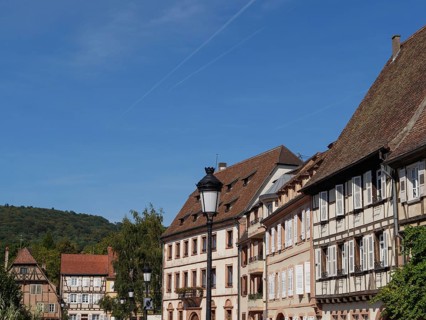 Town view with half-timbered houses and mountainous landscape in the background under a blue sky,