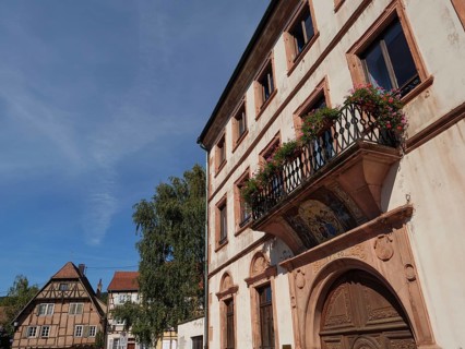 Historic building with balcony and flower boxes under a blue sky in a town, Wissembourg, Alsace,