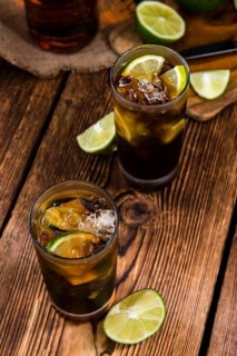 Cuba Libre longdrink with pieces of fresh lime and crushed ice on wooden background