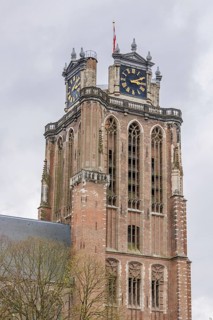 Close-up of a gothic church tower with clocks and a weather vane, dominating the cityscape,
