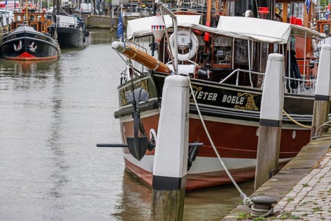 Detailed boat in the harbour, moored to pillars with anchor and white ropes in the foreground,