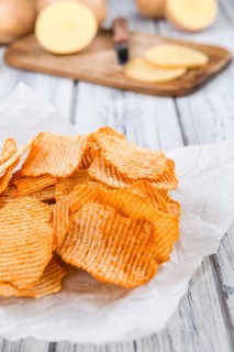 Bowl with rippled Potato Chips (selective focus) on wooden background