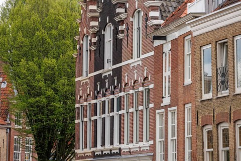 A group of historic brick buildings with detailed facades and trees in the background, Dordrecht,