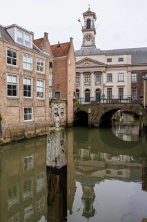 Historic buildings and bridge with clock tower over a quiet canal, reflecting in the water,