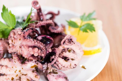 Portion of Octopus Salad (with fresh herbs and garlic) on wooden background
