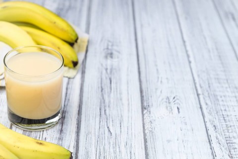 Glass of Banana Juice (close-up shot) on wooden background