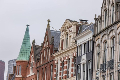 A row of historic townhouses with different facades and roof shapes under a cloudy sky, The Hague,