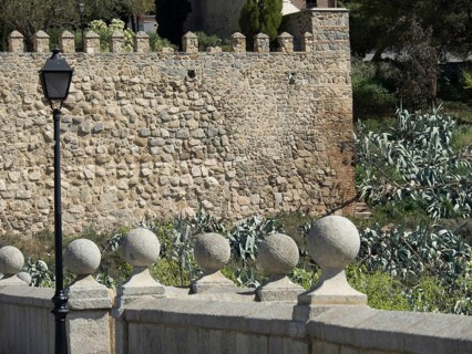 Historic stone wall with a lantern on a bridge surrounded by green vegetation, Toledo, Spain,