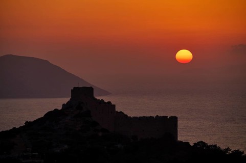 Castle ruins as a silhouette at sunset with a view of the sea and mountains, dark sky, Kritinia